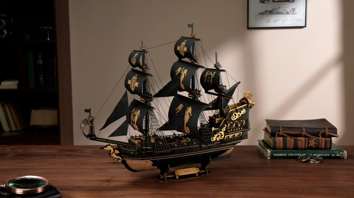 Puzzle 3D : Galion Noir et Or en Bois, modèle assemblé sur un bureau en noyer, voiles noires